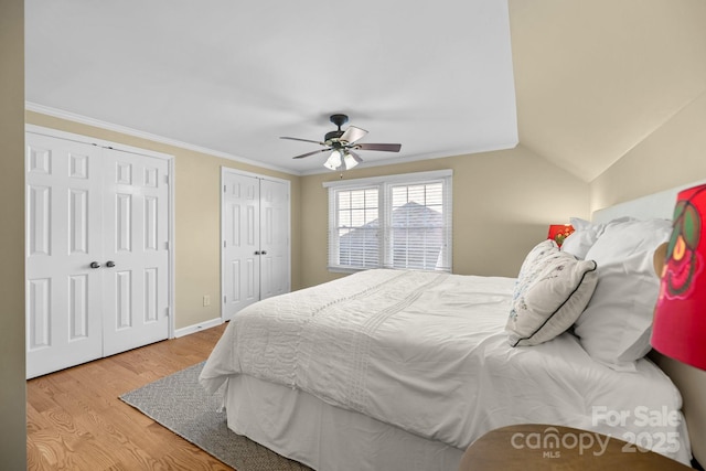 bedroom with baseboards, a ceiling fan, wood finished floors, crown molding, and two closets