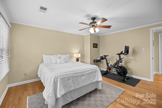 bedroom with visible vents, light wood-style floors, ornamental molding, a ceiling fan, and baseboards