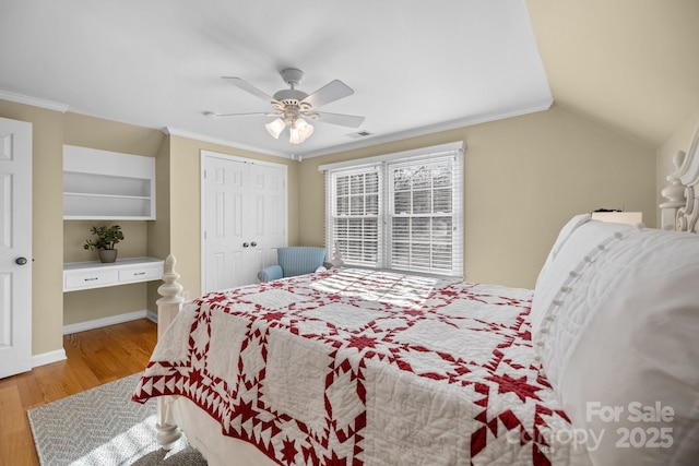 bedroom with wood finished floors, a ceiling fan, vaulted ceiling, ornamental molding, and built in desk