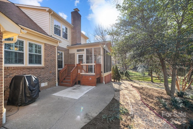 rear view of house with brick siding, a chimney, a sunroom, a patio area, and crawl space