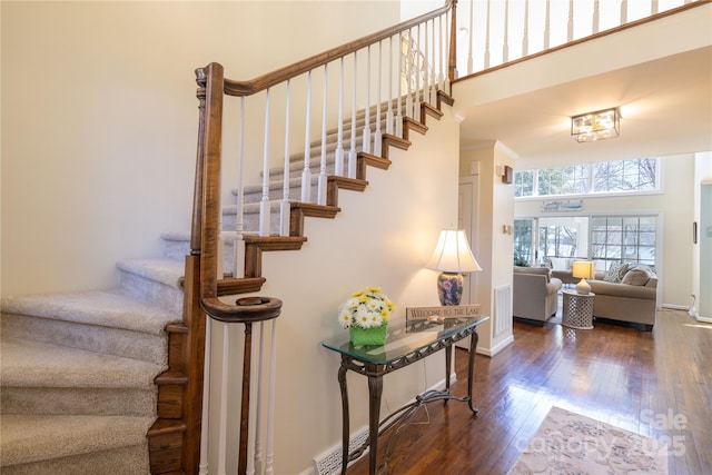 staircase with a towering ceiling, baseboards, and hardwood / wood-style floors