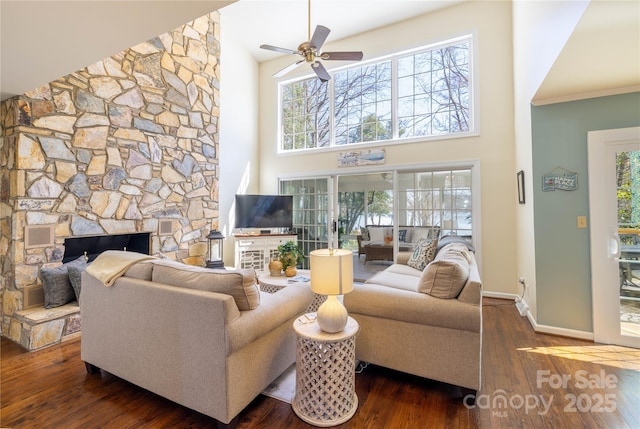 living area with visible vents, a high ceiling, a stone fireplace, wood finished floors, and baseboards