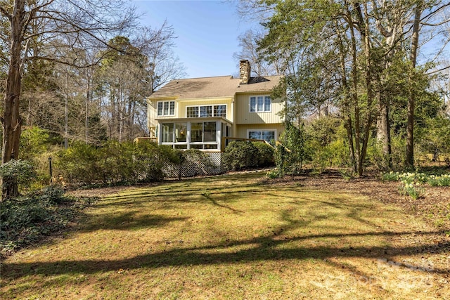 rear view of property featuring a yard, a chimney, and a sunroom