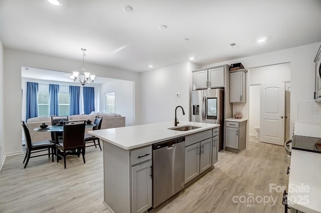 kitchen with gray cabinetry, stainless steel appliances, a sink, light wood-type flooring, and a center island with sink