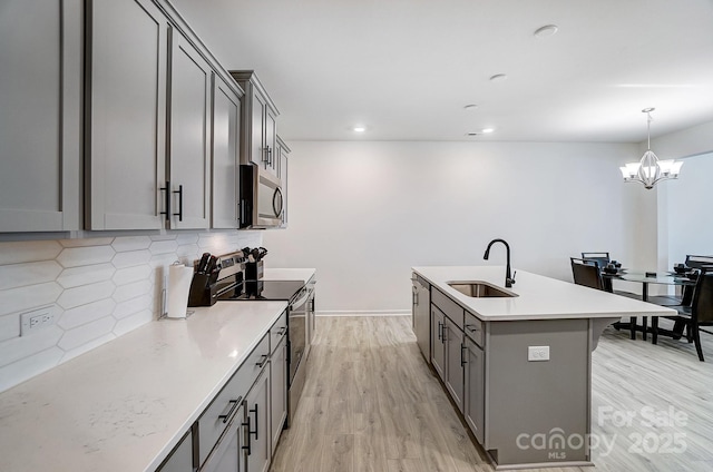 kitchen featuring stainless steel appliances, a sink, light wood-type flooring, gray cabinets, and decorative backsplash