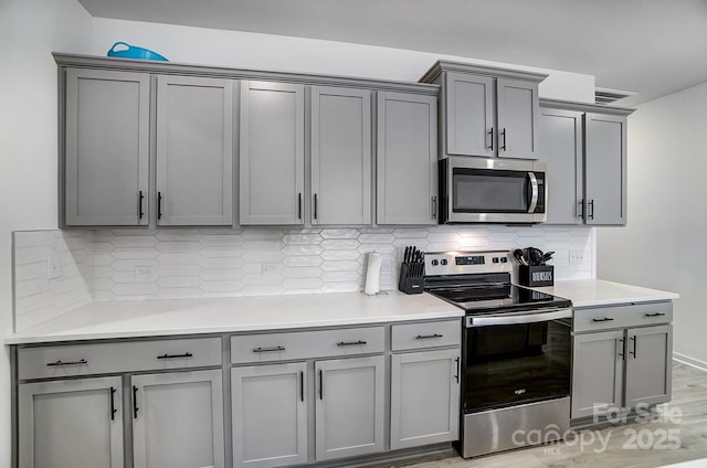 kitchen featuring stainless steel appliances, light countertops, gray cabinets, light wood finished floors, and tasteful backsplash