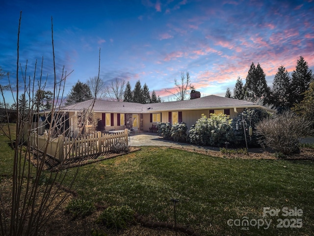 back of property at dusk featuring a lawn, a chimney, and a patio