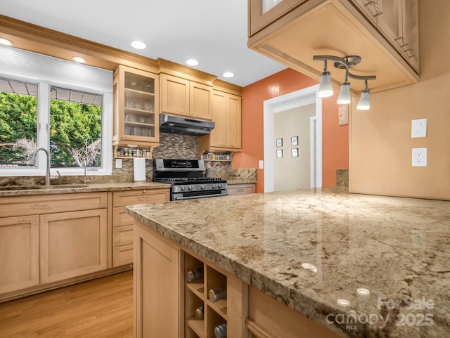 kitchen featuring light brown cabinets, a sink, light stone countertops, under cabinet range hood, and stainless steel gas range oven