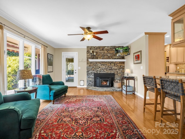 living area featuring a fireplace, a ceiling fan, baseboards, light wood finished floors, and crown molding