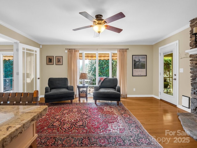 living area with a fireplace, wood finished floors, a ceiling fan, baseboards, and crown molding