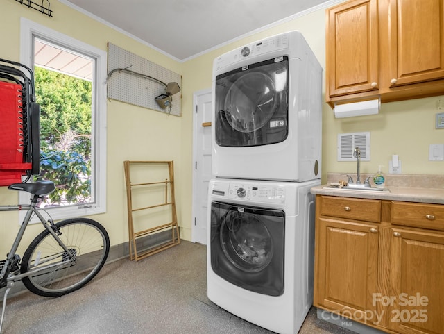 laundry area with a sink, baseboards, cabinet space, stacked washer and clothes dryer, and crown molding