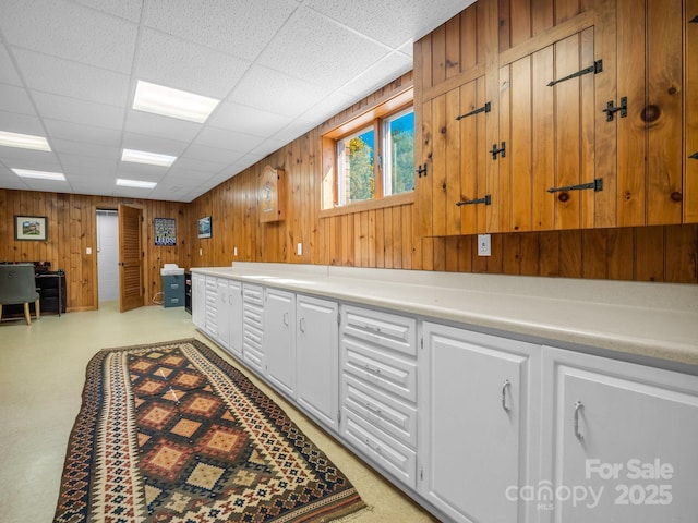 interior space featuring light countertops, white cabinetry, wooden walls, and a drop ceiling