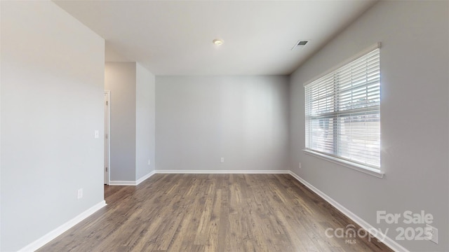 empty room featuring baseboards, visible vents, and dark wood finished floors