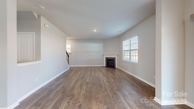 unfurnished living room with a fireplace with flush hearth, dark wood finished floors, and baseboards