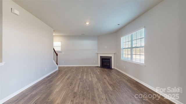 unfurnished living room featuring stairway, a fireplace with flush hearth, baseboards, and wood finished floors