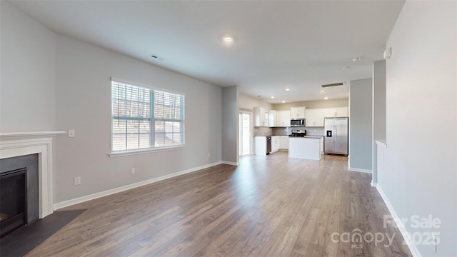 unfurnished living room featuring wood finished floors, a fireplace with flush hearth, visible vents, and baseboards