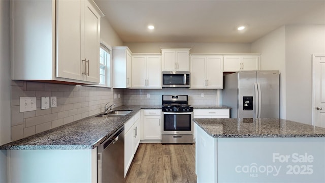 kitchen with light wood-style flooring, stainless steel appliances, a sink, white cabinetry, and decorative backsplash