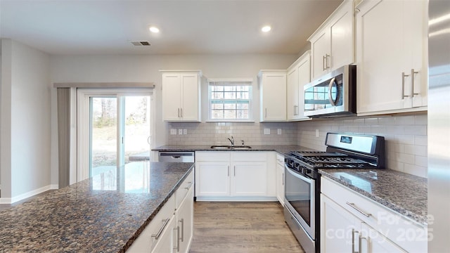 kitchen featuring visible vents, dark stone countertops, stainless steel appliances, white cabinetry, and a sink