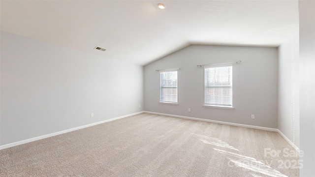 spare room with lofted ceiling, visible vents, light carpet, and baseboards