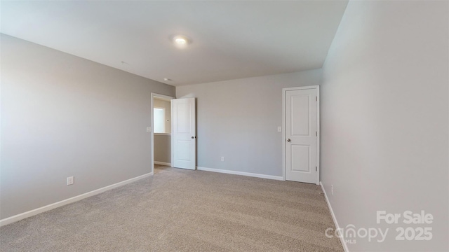 spare room featuring light carpet and baseboards