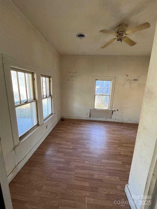 empty room with ceiling fan, dark wood-type flooring, visible vents, baseboards, and crown molding