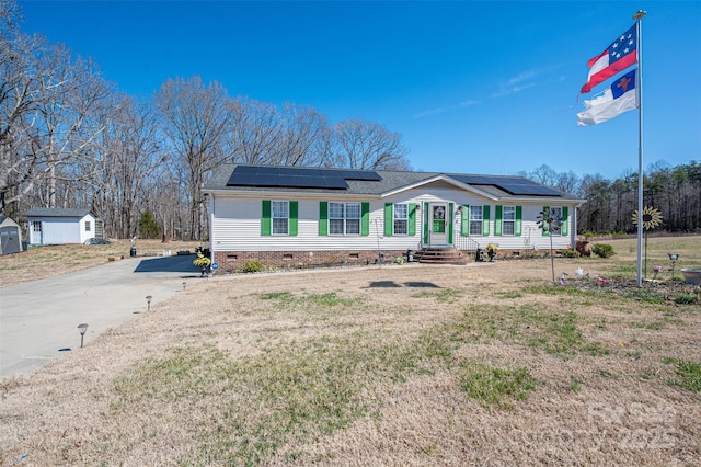 ranch-style home featuring crawl space, roof mounted solar panels, a front lawn, driveway, and an outdoor structure