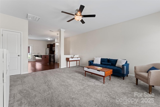 living room featuring dark colored carpet, visible vents, baseboards, and a ceiling fan