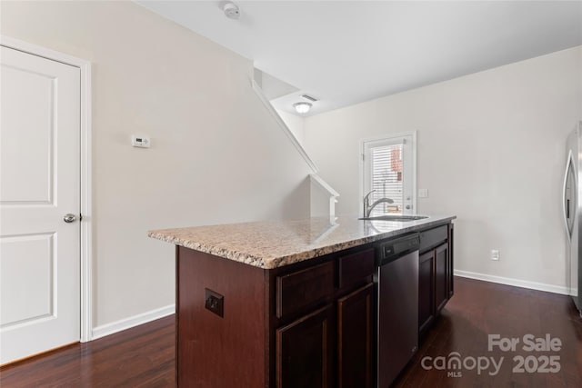 kitchen featuring baseboards, a center island with sink, dark wood-style floors, stainless steel appliances, and a sink