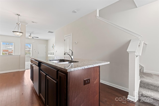 kitchen with light stone countertops, a center island with sink, a sink, dark brown cabinetry, and stainless steel dishwasher