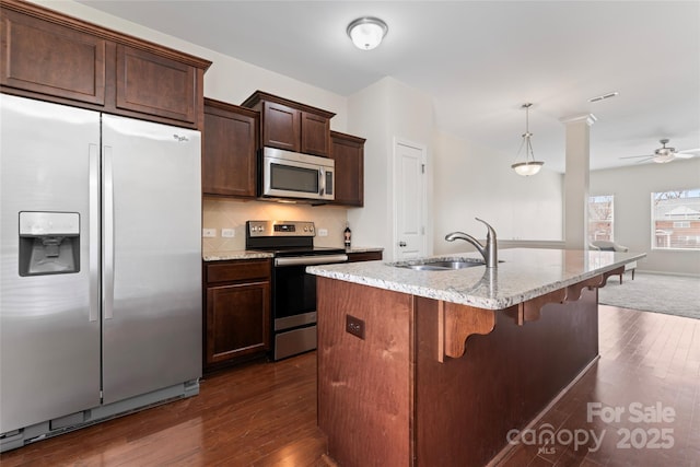 kitchen featuring light stone countertops, a sink, dark wood-type flooring, appliances with stainless steel finishes, and tasteful backsplash