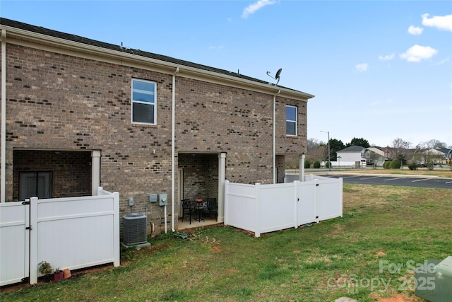 view of property exterior with fence, central AC unit, brick siding, and a lawn