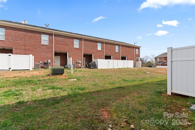 back of house with brick siding, central air condition unit, a yard, and fence