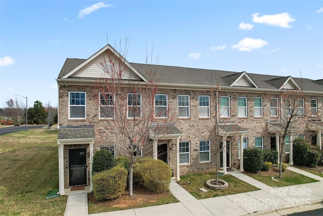 multi unit property with brick siding, a front lawn, and a shingled roof