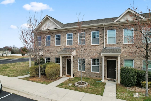 multi unit property with brick siding, a front yard, and a shingled roof