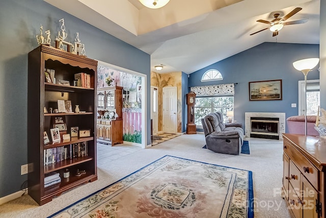 sitting room with lofted ceiling, light colored carpet, a glass covered fireplace, ceiling fan, and baseboards