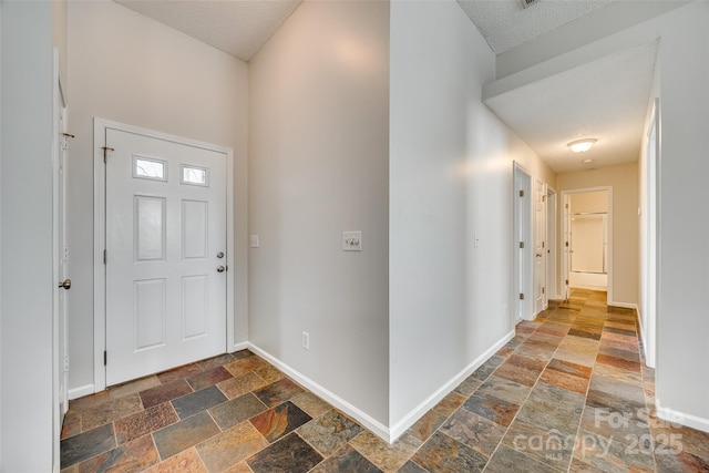 entrance foyer with a textured ceiling, stone tile flooring, and baseboards