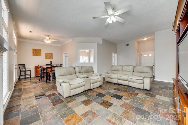 living room featuring ornamental molding, stone finish floor, ceiling fan, and a textured ceiling