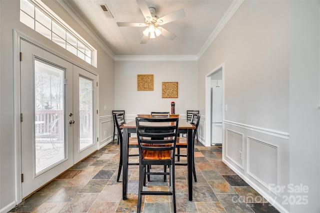 dining area with stone tile floors, visible vents, ornamental molding, french doors, and wainscoting