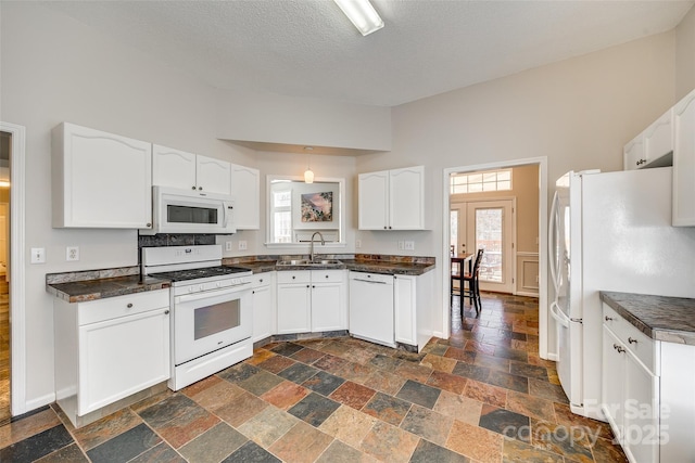 kitchen featuring dark countertops, white appliances, stone tile floors, and a sink