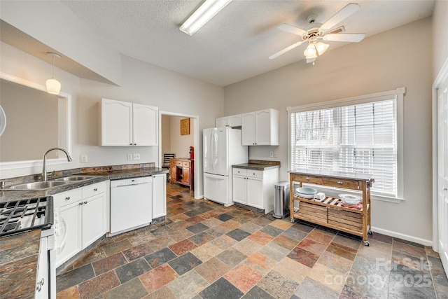 kitchen featuring dark countertops, white appliances, stone finish floor, and a sink