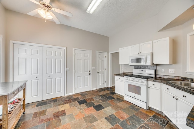 kitchen featuring dark countertops, white appliances, white cabinetry, and stone finish floor