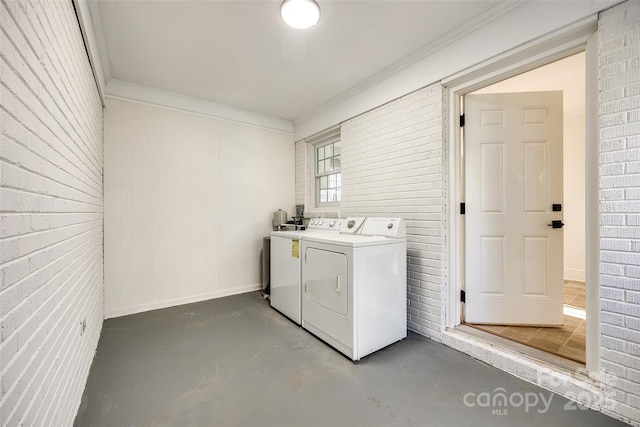 clothes washing area with crown molding, brick wall, separate washer and dryer, laundry area, and baseboards