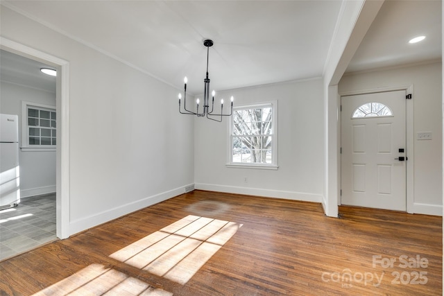 interior space with baseboards, a notable chandelier, wood finished floors, and crown molding