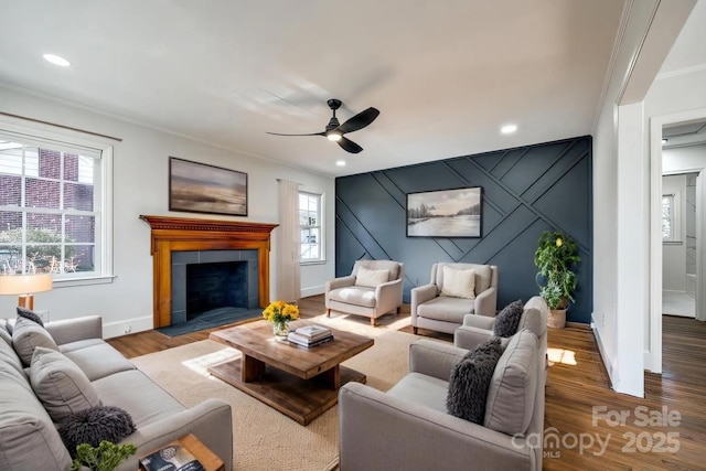 living area featuring crown molding, a tiled fireplace, an accent wall, wood finished floors, and baseboards