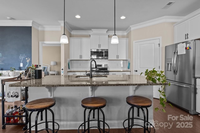 kitchen featuring visible vents, appliances with stainless steel finishes, white cabinets, a sink, and dark stone counters