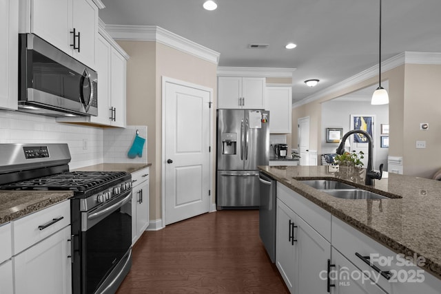 kitchen featuring white cabinets, dark stone counters, ornamental molding, stainless steel appliances, and a sink