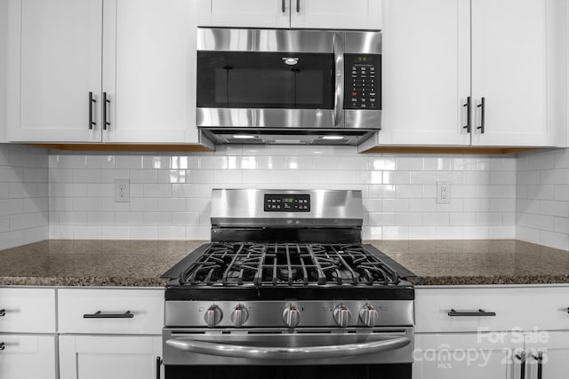 kitchen featuring white cabinetry, stainless steel appliances, backsplash, and dark stone counters