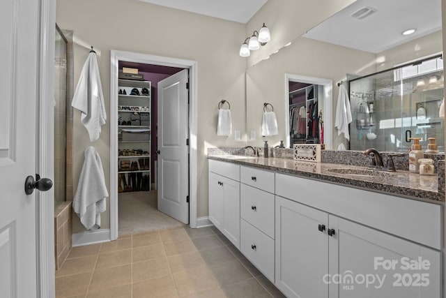 full bath featuring double vanity, tile patterned flooring, a sink, and a shower stall