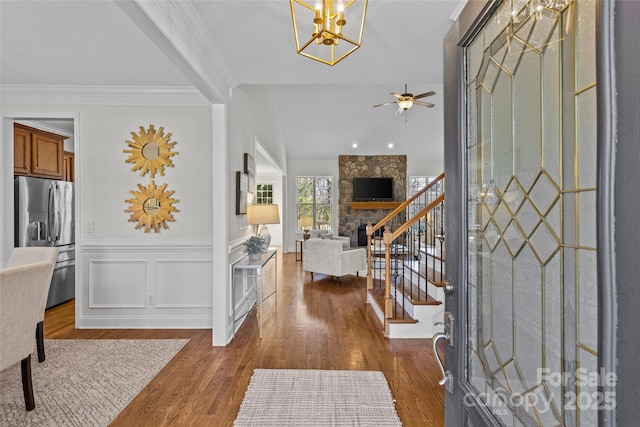 foyer featuring a wainscoted wall, crown molding, a decorative wall, dark wood-type flooring, and stairs