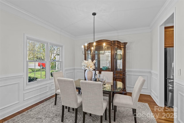 dining space featuring a wainscoted wall, wood finished floors, crown molding, a decorative wall, and a notable chandelier